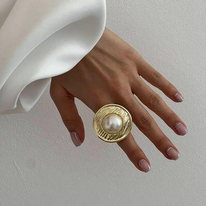 Gold circular ring with a hammered texture and a white pearl in the middle.