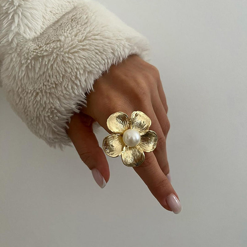 Gold flower-shaped ring with a textured design and a central white pearl.