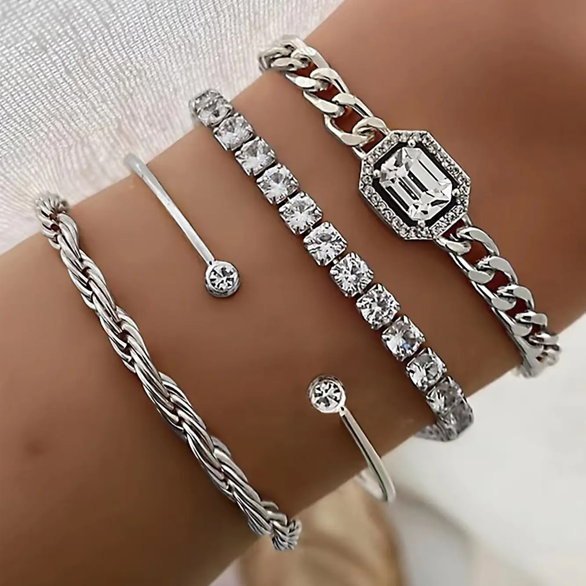 Stackable bracelet set featuring silver designs with twisted rope, bar, tennis, and emerald-cut chain bracelets adorned with cubic zirconia stones.