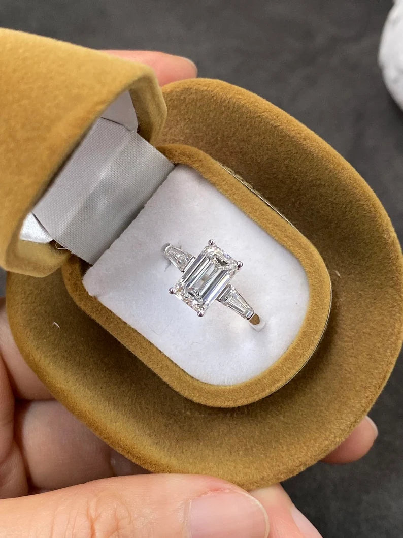 A minimalist three-stone emerald-cut lab-grown diamond ring with two dazzling side stones, set in 18K solid gold, perfect for engagements and weddings.